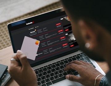 Mann holder et bankkort med laptop foran seg som viser Betsafe bettingside.